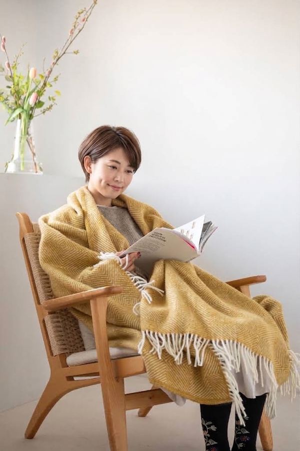 黄色のブランケットを肩に掛けて椅子で雑誌を読む人