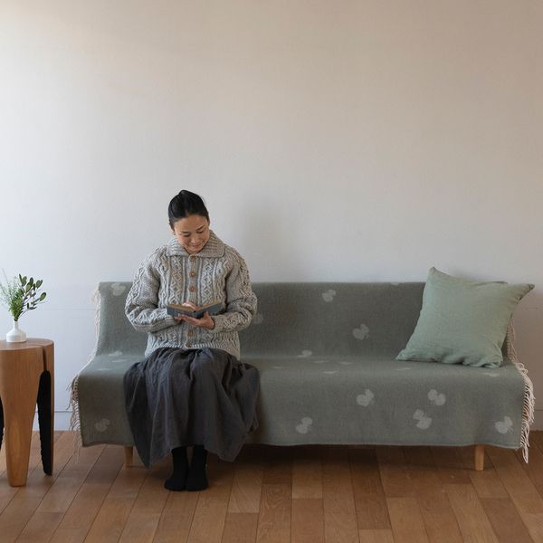 オリーブのCHOUCHOのスローを掛けたソファで本を読む人