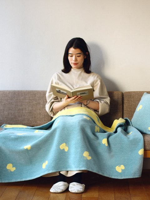 CHOUCHOのハーフブランケットをひざに掛けてソファで本を読む人