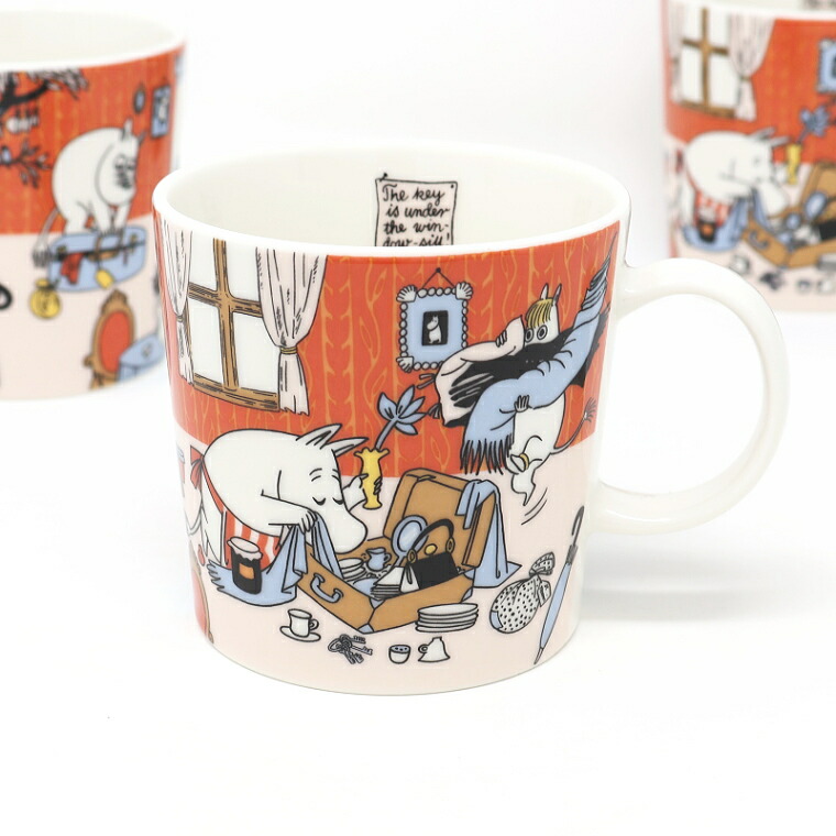 朱色の壁の部屋で、開いたトランクに荷物を詰めるムーミンたちが描かれたマグカップ