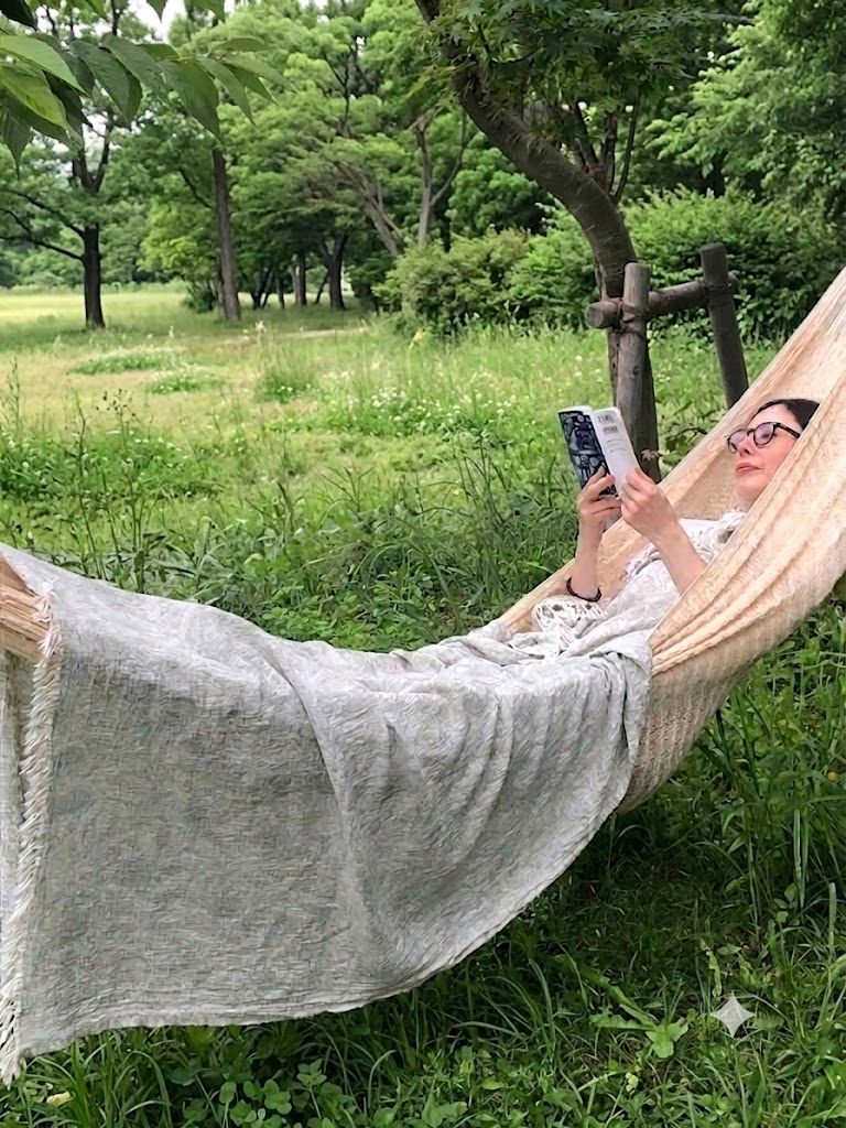 木陰のハンモックにKLIPPANのコットンブランケットを掛けて本を読んでいるところ