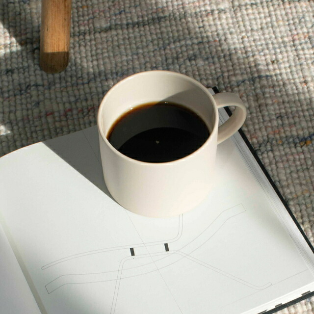白いマグカップにコーヒーを注いだところ。開いた本の上に置かれている