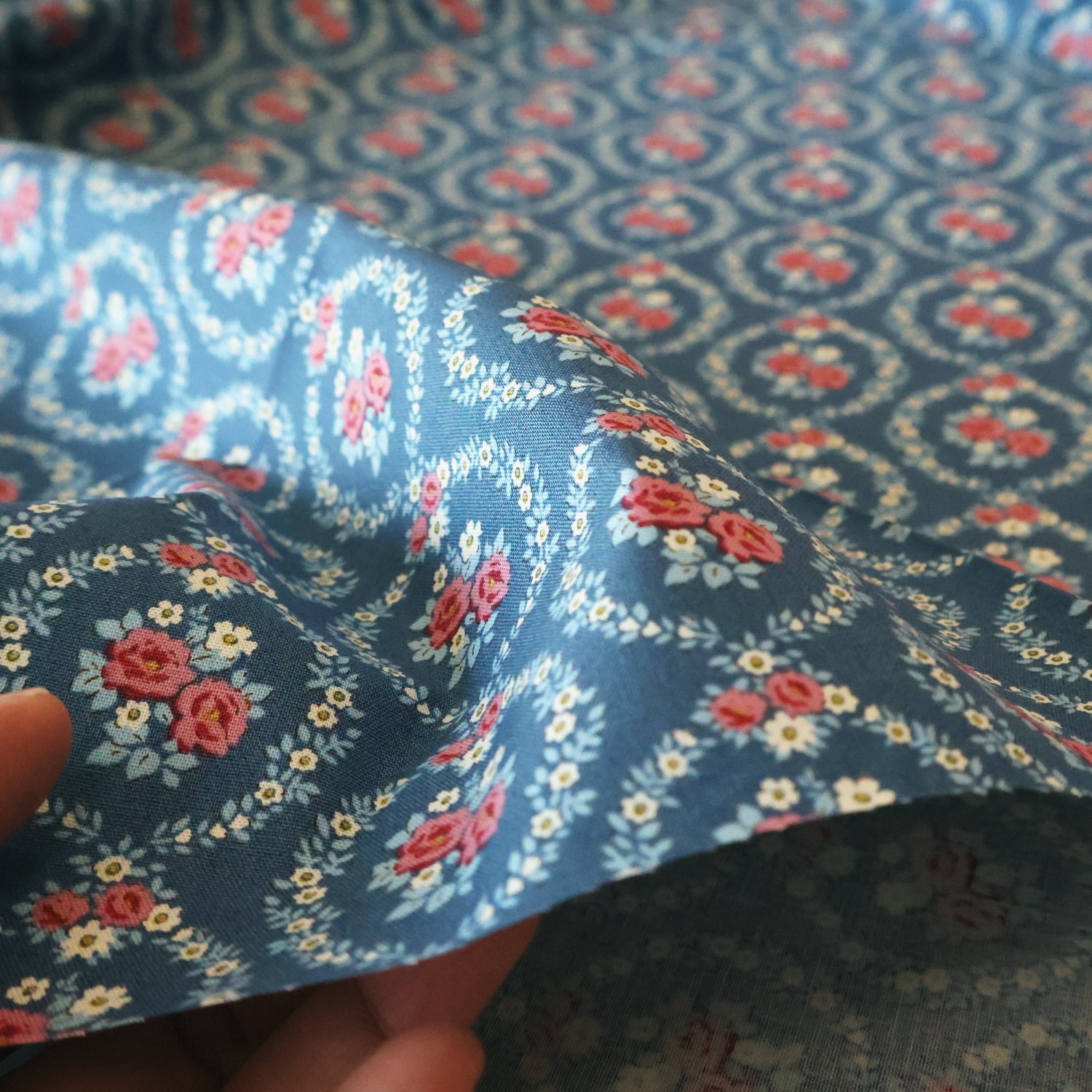 Mable Blue 生地を手に取ったところ。花輪の中の赤いバラ