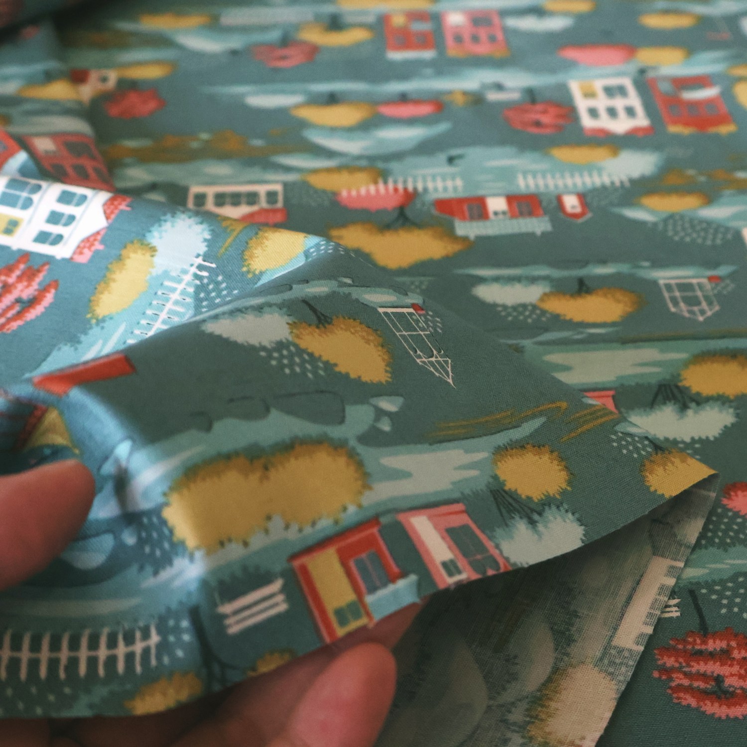 Village Teal 生地を手に取ったところ。家と木々が見える